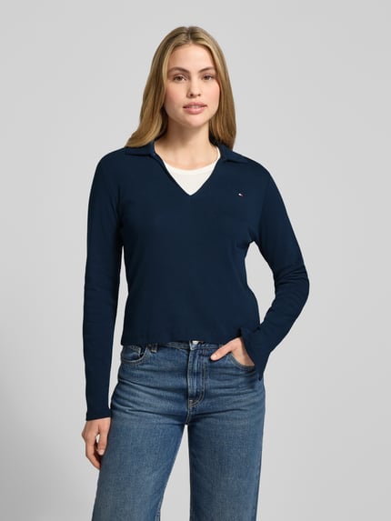 Vrouwenmodel draagt Slim Fit Langarmshirt aus reiner Baumwolle van Tommy Hilfiger, effen donkerblauw, lange mouwen, V-hals, logo detail, voorkant volledig zichtbaar, Ganzkörperansicht von vorne.