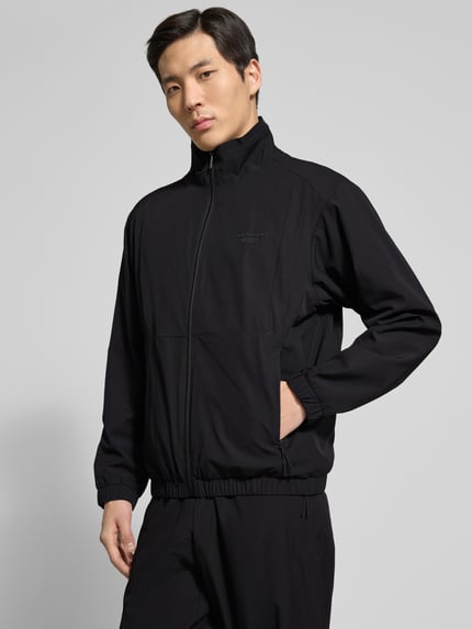Männermodel trägt Regular Fit Trainingsanzug mit Label-Detail Modell LW_PS Spirit70 TT - PORSCHE X BOSS von BOSS Green in Schwarz, Ganzkörperansicht von vorne.