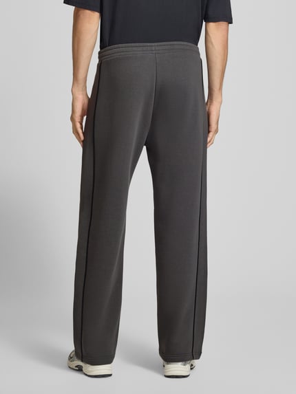 Männermodel trägt Straight Fit Sweatpants aus reiner Baumwolle mit Label-Patch von REVIEW, dunkelgrau, elastischer Bund, Eingrifftaschen, Ganzkörperansicht Rückansicht.