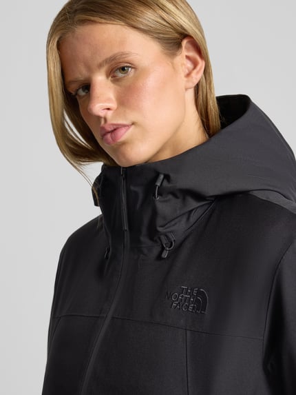 Frauenmodel trägt Jacke mit Logo-Stitching Modell 'RANGE DOWN' von The North Face in Schwarz, glatte Oberfläche, Nahaufnahme Oberkörper. Damen Jacke, gerader Schnitt, Kapuze mit Tunnelzug, seitliche Eingrifftaschen, Klettverschluss am Ärmel.