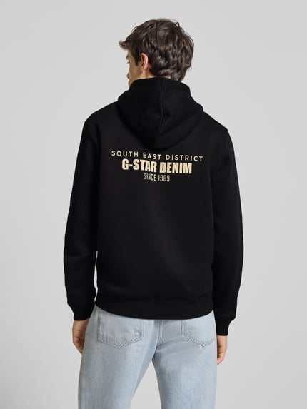 Männermodel trägt Hoodie mit Kapuze von G-Star Raw in Schwarz mit Label-Print und Känguru-Tasche, Baumwoll-Mix, Rückenansicht.