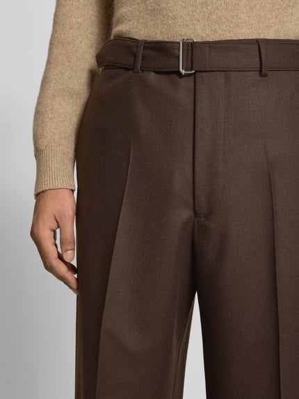 Männermodel trägt Regular Fit Bundfaltenhose aus Schurwolle von Officine Générale in Braun mit Struktur, seitlichen Taschen und Gürtelschlaufen, Nahaufnahme Oberkörper.