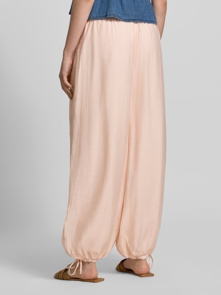 Frauenmodel trägt Relaxed Fit Stoffhose aus Viskose-Mix von Gina Tricot, semitransparentes Design, elastischer Bund mit Tunnelzug, eingefasste Ärmelabschlüsse, Bundweite bei Größe S: 39 cm, Innenbeinlänge bei Größe S: 73 cm, Ganzkörperansicht Rückansicht.