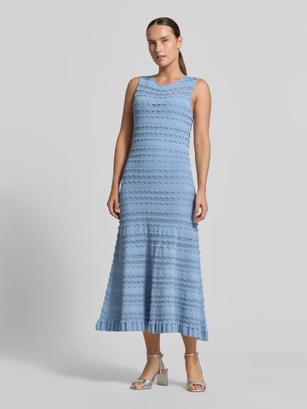 Kobiece modelka nosi sukienkę midi z mieszanki wiskozy, dopasowany krój, imitacja dzianiny, obszycie falbanami, model 'Cahrlie' Ted Baker, jasnoniebieska, widok całej sylwetki z przodu. Długość tyłu w rozmiarze 36: 120 cm, szerokość w rozmiarze 36: 43 cm.