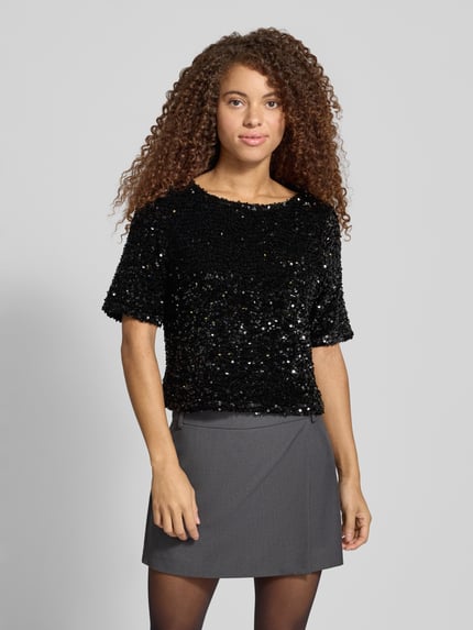 Frauenmodel trägt Blusentop mit Allover-Pailletten von PIECES, dunkle Töne, Rundhals, 1/2-Arm, abgerundeter Abschluss, Ganzkörperansicht von vorne.