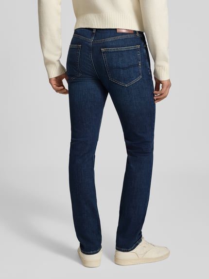 Męski model nosi Slim Fit Jeans aus Baumwoll-Mix Modell 'Hatch' od Pepe Jeans, ciemnoniebieski denim, wyraźne szwy, tekstura gładka, pełny tył. Jeansy męskie krój slim fit. Ganzkörperansicht Rückansicht.