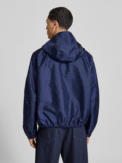 Männermodel trägt Regular Fit Windbreaker mit Zweiwege-Reißverschluss von Kenzo in Dunkelblau mit Jacquard-Muster, Rückenansicht, Herrenmodell, elastische Abschlüsse, Kapuze, Ärmeltasche mit Reißverschluss