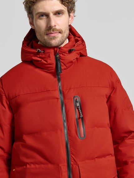 Männermodel trägt Steppjacke mit Pattentaschen von camel active in Rot, Kapuze, Reißverschluss, sichtbare Brusttasche, Nahaufnahme Oberkörper. Kontext: Herren Steppjacke, gerade Passform, Kapuze mit Tunnelzug, Reißverschlüsse, Rückenlänge 80 cm, Schulterbreite 51 cm, Brustweite 64 cm, Ärmellänge 67 cm.