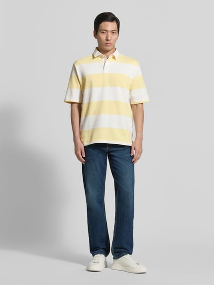 Männermodel trägt Relaxed Fit Poloshirt im Allover-Look von MCNEAL aus Baumwoll-Mix, gelb-weiß gestreift, Knopfleiste, Rückenlänge 70 cm, Ganzkörperansicht von vorne.