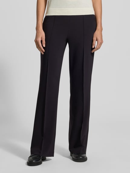 Frauenmodel trägt Regular Fit Hose mit Gummizugbund Ava von CAMBIO, schwarze Jersey-Optik mit Bundfalten und Logo, Nahaufnahme Oberkörper.