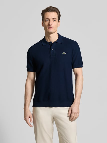 Männermodel trägt Regular Fit Poloshirt aus reiner Baumwolle von Lacoste, Optik: Unifarben, Logo-Stitching, Polokragen, Kurzarm, Materialverarbeitung: Querstrick, Ganzkörperansicht von vorne.
