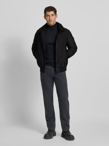 Männermodel trägt schwarze Bomberjacke mit Stehkragen Modell 'Ginster' von khujo, Material-Mix, Ganzkörperansicht von vorne.