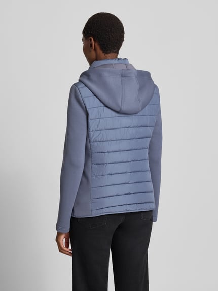 Frauenmodel trägt Steppjacke mit Kapuze und Reißverschlusstaschen von Christian Berg Woman Selection in Blau, glatte und gesteppte Texturen, Ganzkörperansicht Rückansicht. Rückenlänge 59 cm, Schulterbreite 41 cm, Brustweite 50 cm, Ärmellänge 65 cm, Regular Fit.