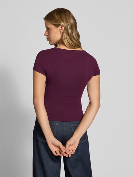 Frauenmodel trägt Slim Fit T-Shirt aus reiner Baumwolle von Tommy Jeans in dunklem Violett, glatte Textur, Ganzkörperansicht Rückansicht. Damen T-Shirt von Tommy Jeans.