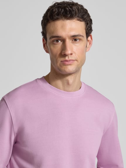 Männermodel trägt Regular Fit Sweatjacke aus reiner Baumwolle von Marc O'Polo in Uni-Rosa mit Label Print, Nahaufnahme Oberkörper.