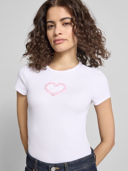 Kobiece model prezentuje damski t-shirt z mieszanki bawełny z dodatkiem streczu, prosty krój, model 'PREPPY HEART' od Review, okrągły dekolt, drobne prążkowanie, długość tyłu w rozmiarze S: 49 cm, całkowity widok z przodu.