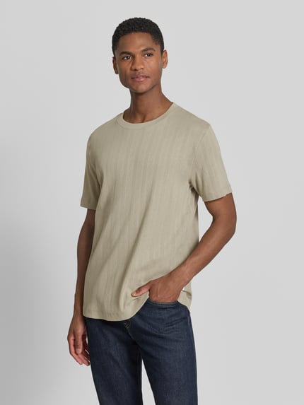 Männermodel trägt T-Shirt in Jaquard-Strick mit Rundhalsausschnitt von Lindbergh aus Reine Baumwolle, Regular-Fit, Label-Detail, Rückenlänge 72 cm, sandfarben, dezentes Jaquard-Muster, Ganzkörperansicht von vorne.