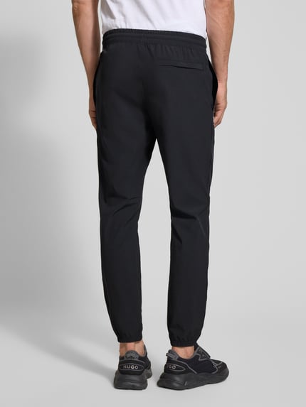 Männermodel trägt Regular Fit Sweatpants mit Logo-Print Modell 'Vibe' von Under Armour, schwarzer Elastischer-Material-Mix, Gesäßtasche, Elastikbund, Ganzkörperansicht Rückansicht.