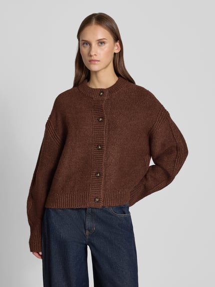 Frauenmodel trägt Boxy Fit Strickjacke Modell 'FLORA' von Topshop in Braun mit Knopfleiste, lockerer Schnitt, Jeans, Ganzkörperansicht von vorne. Damen Strickjacke mit Rundhalsausschnitt, Rückenlänge 54 cm, Ärmellänge 53 cm.