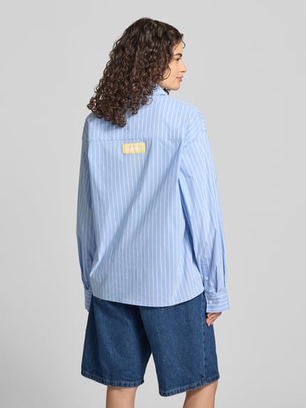Frauenmodel trägt Relaxed Fit Bluse mit Label-Print von ANOTHER COTTON LAB in Hellblau mit weißen Streifen aus reiner Baumwolle, Ganzkörperansicht Rückansicht.