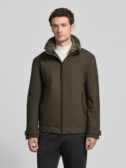 Männermodel trägt Daunenjacke mit abnehmbarem Kapuzeneinsatz von Strellson in matt-oliv, dezente Struktur, Reißverschlüsse, Ganzkörperansicht von vorne.
