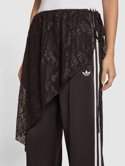 Kobieta nosi Loose Fit Sweathose aus Baumwoll-Mix model '2IN1 LACE FIREBIRD' od adidas Originals, czarno-białe kolory, koronka i gładka tekstura, zbliżenie na biodra i pas.