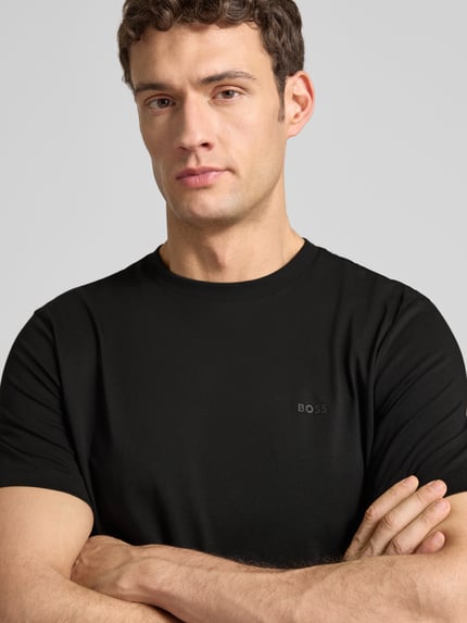 Męski model nosi T-Shirt aus Baumwolle Modell 'Thompson' od BOSS, czarny, logo z przodu, bawełna, prosty krój, zbliżenie na górną część ciała.