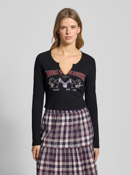 Frauenmodel trägt Cropped Longsleeve mit Label-Print Modell 'BUDDHA' von TRUE RELIGION, Material-Mix mit Viskose-Anteil, Slim Fit, V-Ausschnitt, Frontprint, dunkle Farbe, Rückenlänge bei Größe S: 43 cm, Ganzkörperansicht von vorne.