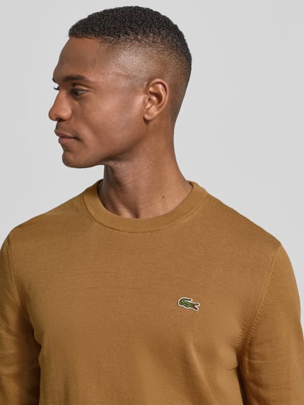 Männermodel trägt Regular Fit Strickpullover aus Baumwoll-Mix von Lacoste, Optik: Unifarben, Label-Patch, Nahaufnahme Oberkörper.