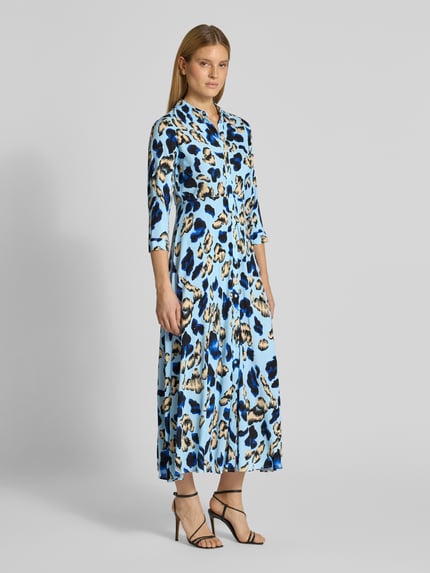 Frauenmodel trägt Hemdblusenkleid aus Viskose Modell 'SAVANNA' von YAS mit blauem, schwarzem und beigem Animal-Print, taillierter Midikleid-Schnitt, Kentkragen, Knopfleiste und 3/4-Ärmeln; Ganzkörperansicht von vorne.