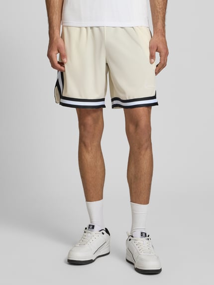 Männermodel trägt Regular Fit Shorts mit elastischem Bund von KARL KANI in Beige mit Strukturmuster und Logo-Stitching, Nahaufnahme Unterkörper. Bundweite 38 cm, Innenbeinlänge 21 cm, Herren Shorts.