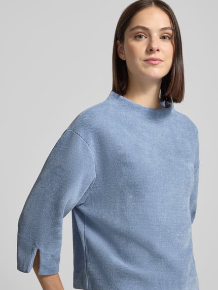 Frauenmodel trägt Relaxed Fit Strickpullover mit Stehkragen von ZABAIONE in hellblauer Strick-Optik, 3/4-Arm, Nahaufnahme Oberkörper.