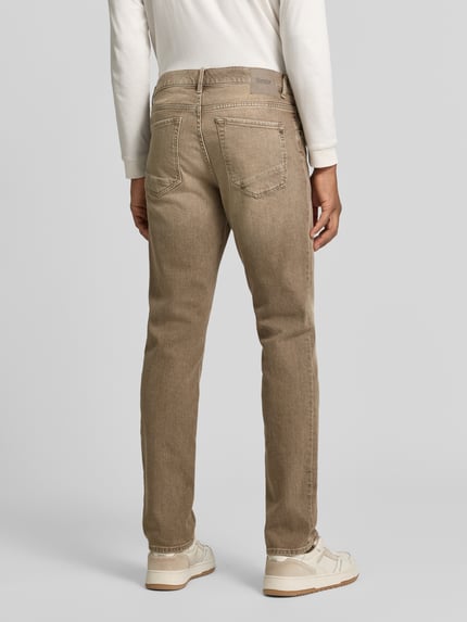 Männermodel trägt beigefarbene Slim Fit Jeans aus Baumwoll-Mix Modell 'Chuck' von Brax, Herren Slim Fit Jeans, Ganzkörperansicht Rückansicht.