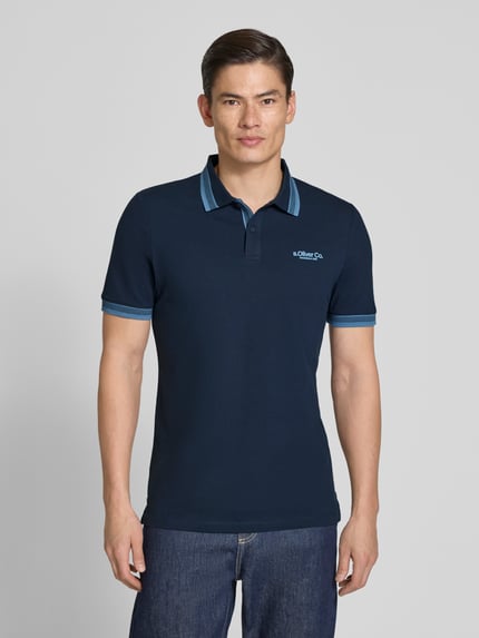 Męski model nosi Regular Fit Poloshirt aus Baumwoll-Mix von s.Oliver RED LABEL, jednolity kolor, bawełniany miks, detal label print, kołnierzyk polo, krótkie rękawy z ściągaczem, dół z bocznymi rozcięciami, faktura pikowana; widok całej sylwetki z przodu.