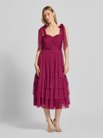 Frauenmodel trägt Knielanges Cocktailkleid im Stufen-Look von LACE & BEADS aus Mesh in A-Linie, Farbe Beere, Drapierungen, Ganzkörperansicht von vorne. Rückenlänge bei Größe S: 104 cm, Brustweite bei Größe S: 40 cm.