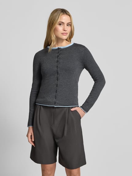 Frauenmodel trägt Strickjacke mit Rundhalsausschnitt Modell 'LUCCAPK' von MANGO in Dunkelgrau, glatte Textur, Nahaufnahme Oberkörper. Material-Mix mit Baumwoll-Anteil, Slim Fit, Knopfleiste, kontrastfarbene Abschlüsse.