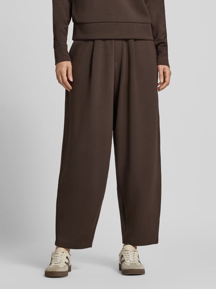 Frauenmodel trägt Barrel Fit Sweatpants mit elastischem Bund von Christian Berg Woman, braun, weite Form, glatte Textur, Ganzkörperansicht von vorne. Material-Mix mit Modal-Anteil, Bundfalten.