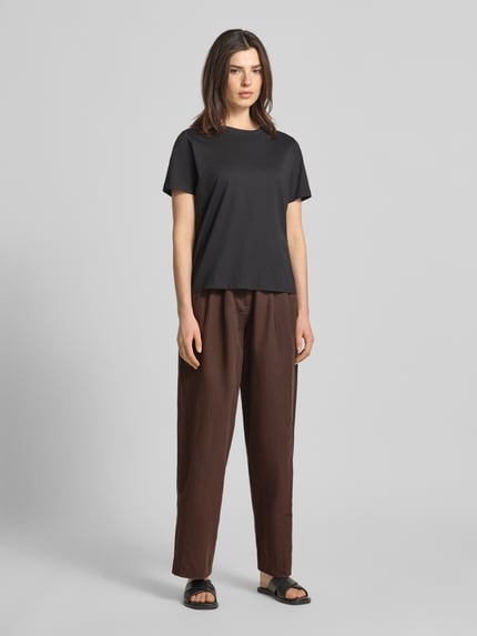 Frauenmodel trägt Wide Leg Hose mit Eingrifftaschen Modell 'QUINN' von Scotch & Soda aus Baumwoll-Leinen-Mix in Braun, Ganzkörperansicht von vorne.