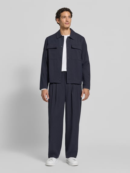 Männermodel trägt Stoffhose mit Bügelfalte Modell 'GRANT' von Casual Friday, dunkle Farbe, straight Fit, Ganzkörperansicht von vorne.