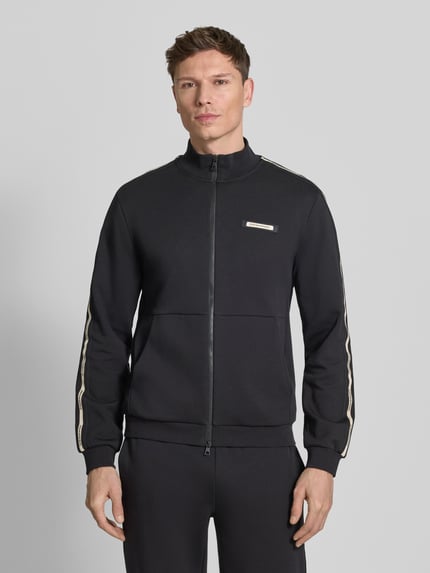Männermodel trägt Sweatjacke mit Stehkragen und Zweiwege-Reißverschluss von EA7 Emporio Armani, schwarz, Regular Fit, Label-Detail, Ganzkörperansicht von vorne.