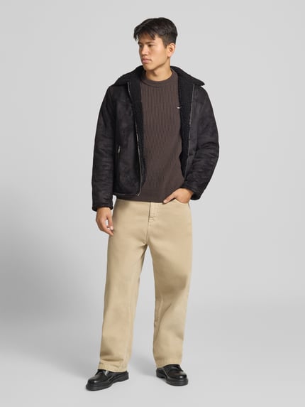 Männermodel trägt Jacke in Leder-Optik mit Reißverschlusstaschen von REVIEW in Schwarz, Regular Fit, Beige Hose, Ganzkörperansicht von vorne.