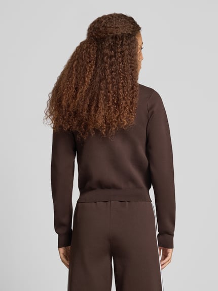 Frauenmodel trägt Strickjacke mit Zweiwege Reißverschluss von adidas Originals in Braun, Strukturmuster, Slim Fit, Ganzkörperansicht Rückansicht.