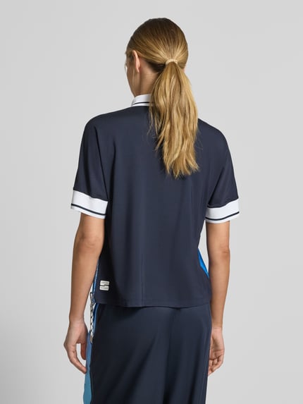 Männermodel trägt Regular Fit Bluse aus reinem Lyocell mit Polokragen von Marc Cain, granatowy, krój regular fit, krótki rękaw, nadruk allover, tunel w talii, długość tyłu w rozmiarze 36: 60 cm, długość rękawa w rozmiarze 36: 39 cm, widok całej sylwetki z tyłu.