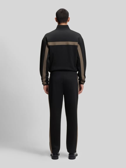 Männermodel trägt Relaxed Fit Jogginghose mit Galonstreifen Modell 'DOLOS' von HUGO, Sweat-Material, unifarben, Ganzkörperansicht Rückansicht.