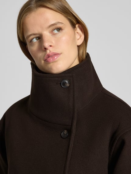 Frauenmodel trägt Jacke mit Stehkragen und Bindegürtel von Gina Tricot in Dunkelbraun, glatte Textur, Nahaufnahme Oberkörper. Rückenlänge 70 cm, Schulterbreite 48 cm, Brustweite 48 cm, Ärmellänge 58 cm, Regular Fit, Knopfverschluss.