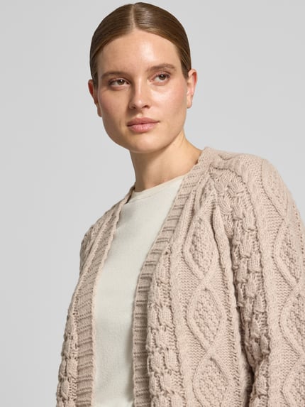 Frauenmodel trägt Longcardigan mit Zopfmuster von Apricot in Beige, offene Front, gerippte Abschlüsse, Nahaufnahme Oberkörper.