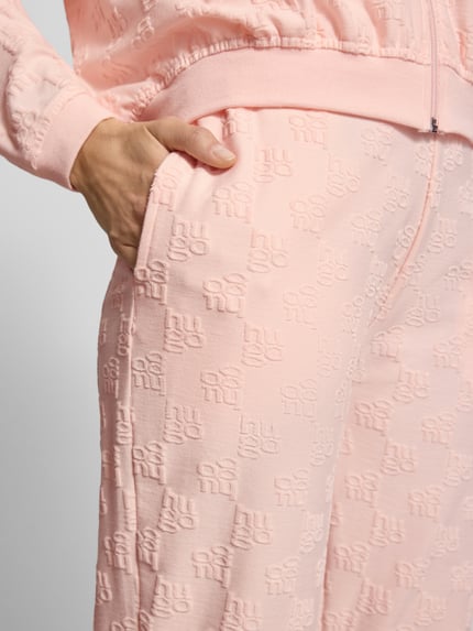 Frauenmodel trägt Slim Fit Sweatpants aus Baumwoll-Mix Modell 'TERRYMONOGRAM' von HUGO in Rosa mit Logo-Monogramm, Nahaufnahme Oberschenkel.
