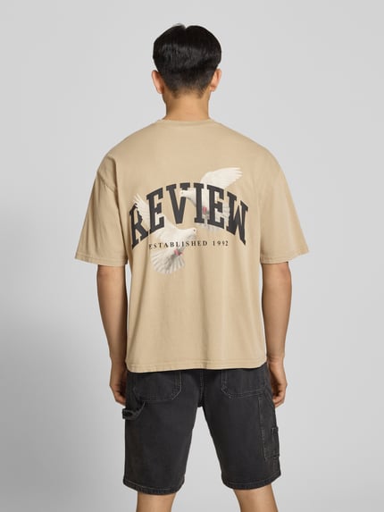 Männermodel trägt T-Shirt mit Logo- und Motiv-Print von REVIEW in Beige, Reine Baumwolle, Loose-Fit, Ganzkörperansicht Rückansicht.