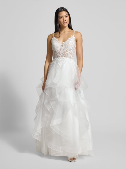Modelka kobieca nosi Brautkleid mit Details aus Spitze od LUXUAR FASHION, białe warstwowe, koronka, materiał wytrzymały, krój taliowany, widok z przodu, cała sylwetka.