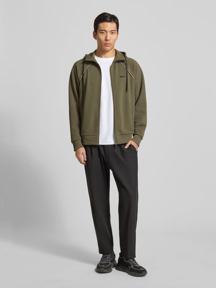 Männermodel trägt Regular Fit Sweatjacke aus Baumwoll-Mix von BOSS Green in Oliv mit Kapuze, Reißverschluss und Piqué-Struktur, Ganzkörperansicht von vorne.